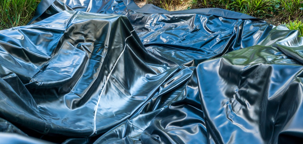 A flexible black pond liner spread across the grass during a backyard installation. The material is bunched up in several areas.