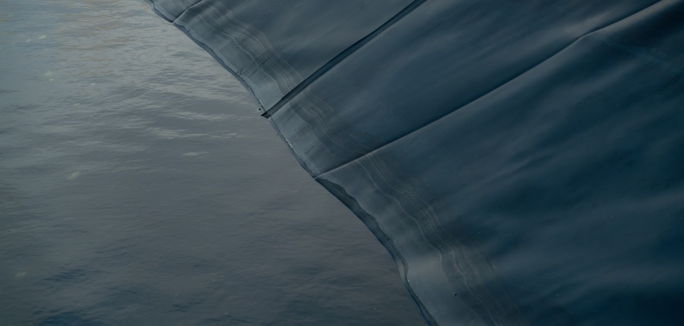 A close-up view shows a black pond liner that contains water. The water is still, and the liner has creases.