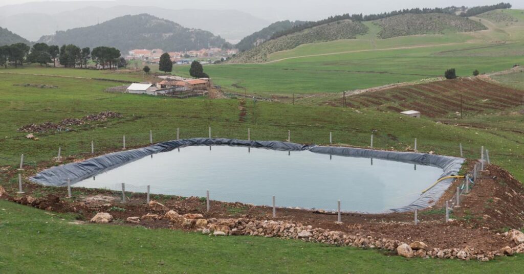 A black pond liner sits underneath a homemade pond that's surrounded by a wire fence with white posts.