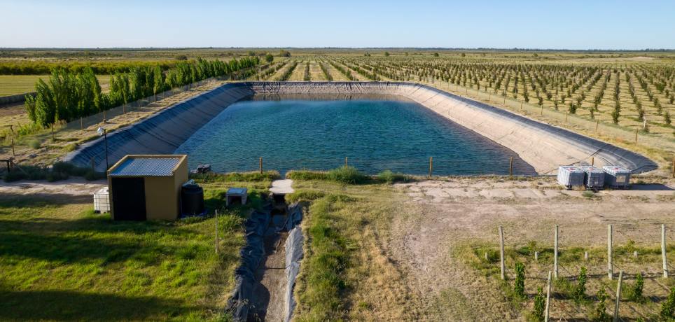 A large water retention pond is half-filled with water and has a black liner. Agriculture land appears around the pond.