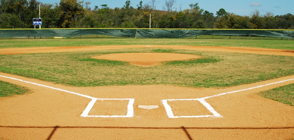 The home plate of the baseball field has fresh paint for the lines and batter's box. A fence is in the outfield.