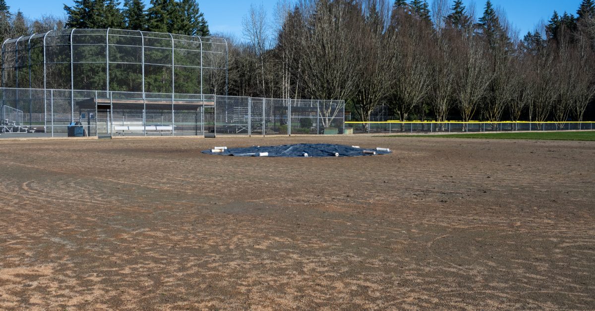 A black tarp covers the pitcher's mound of a baseball field, and gray cinderblocks sit around the edge of the field.