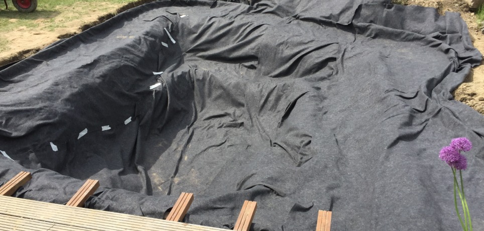 A pond liner is being installed for a small, new pond. A deck is next to the new pond and a pile of dirt.