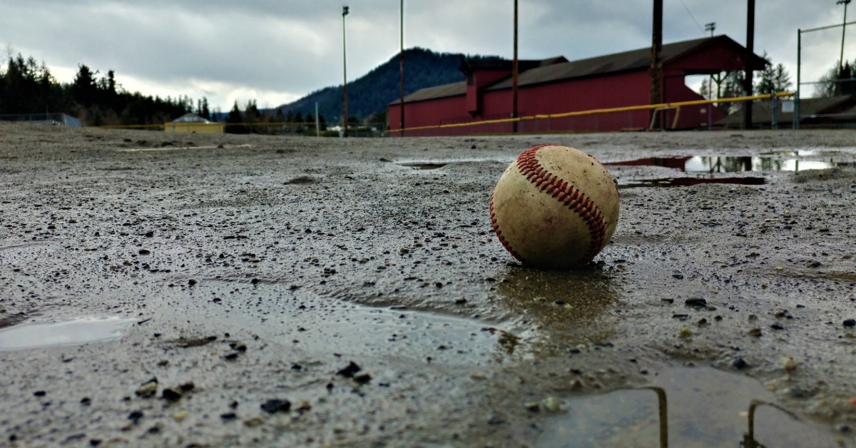A close-up view shows a dirty baseball sitting in a muddy area. There are puddles of water in the mud.