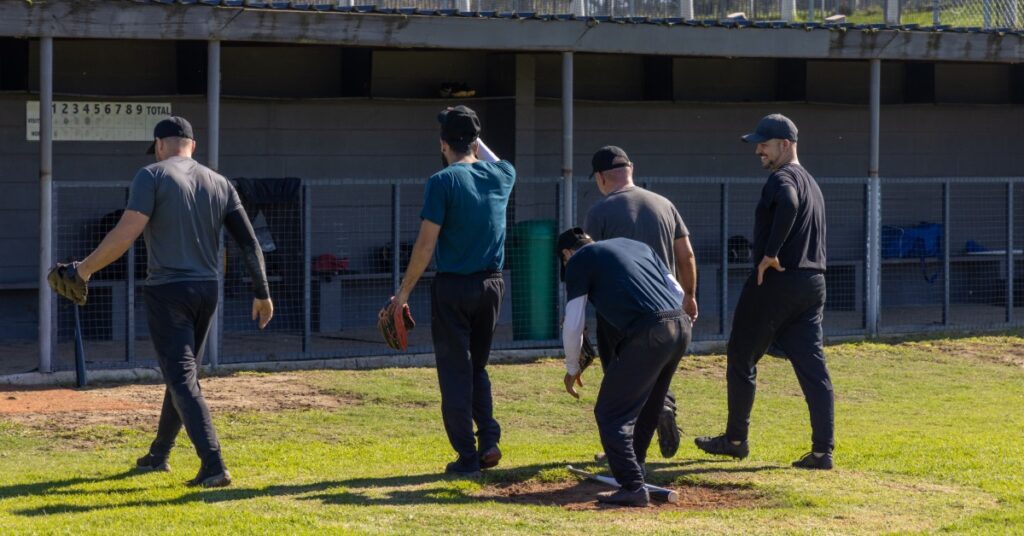 Five men wearing dark shirts, baseball caps, and black pants are walking to a dugout and off the baseball field.