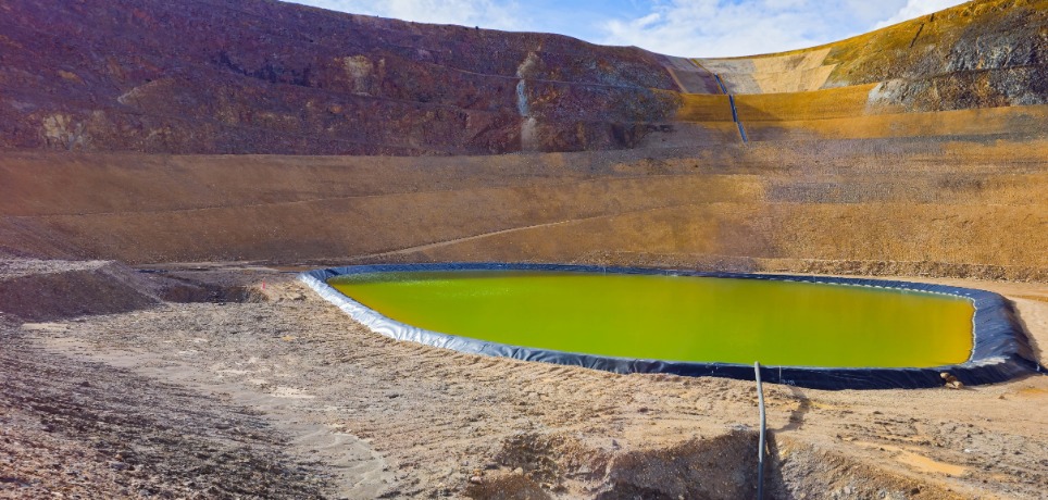 A containment pit is lined with a black liner and is filled with a liquid. A black hose leads to the pit.